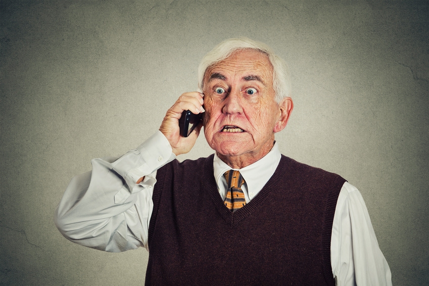 Angry senior man talking on mobile phone gray background